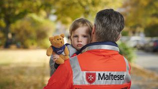 Mitarbeiter in der Krisenintervention trägt Kind mit Teddybär.