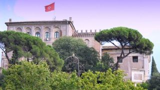 Die Villa Malta hinter Bäumen mit roter Malteser Fahne.