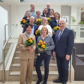 Gruppenfoto auf einer Treppe mehrere Personen halten Blumensträuße ein Mann steht vorn im Anzug.