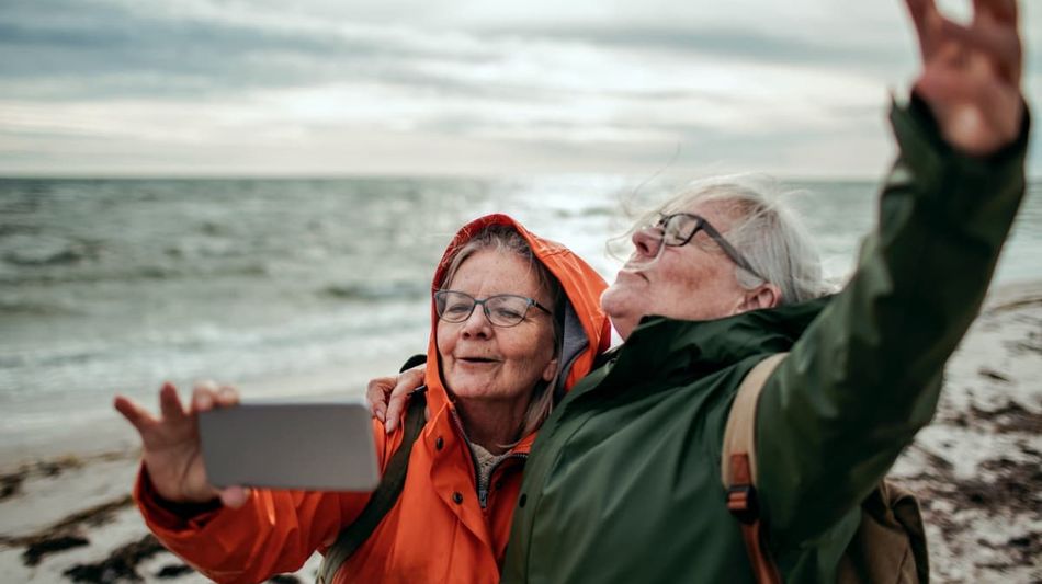 Zwei ältere Damen machen einen Strandspaziergang und fotografieren sich.