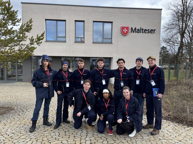 Menschen in Malteser Kleidung stehen vor dem Malteser Haus