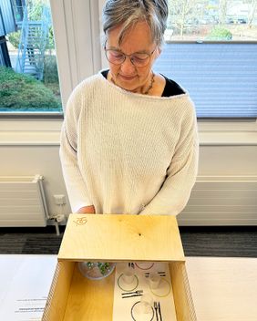 Eine Frau steht vor einem Kasten mit Löffeln und Kugeln.