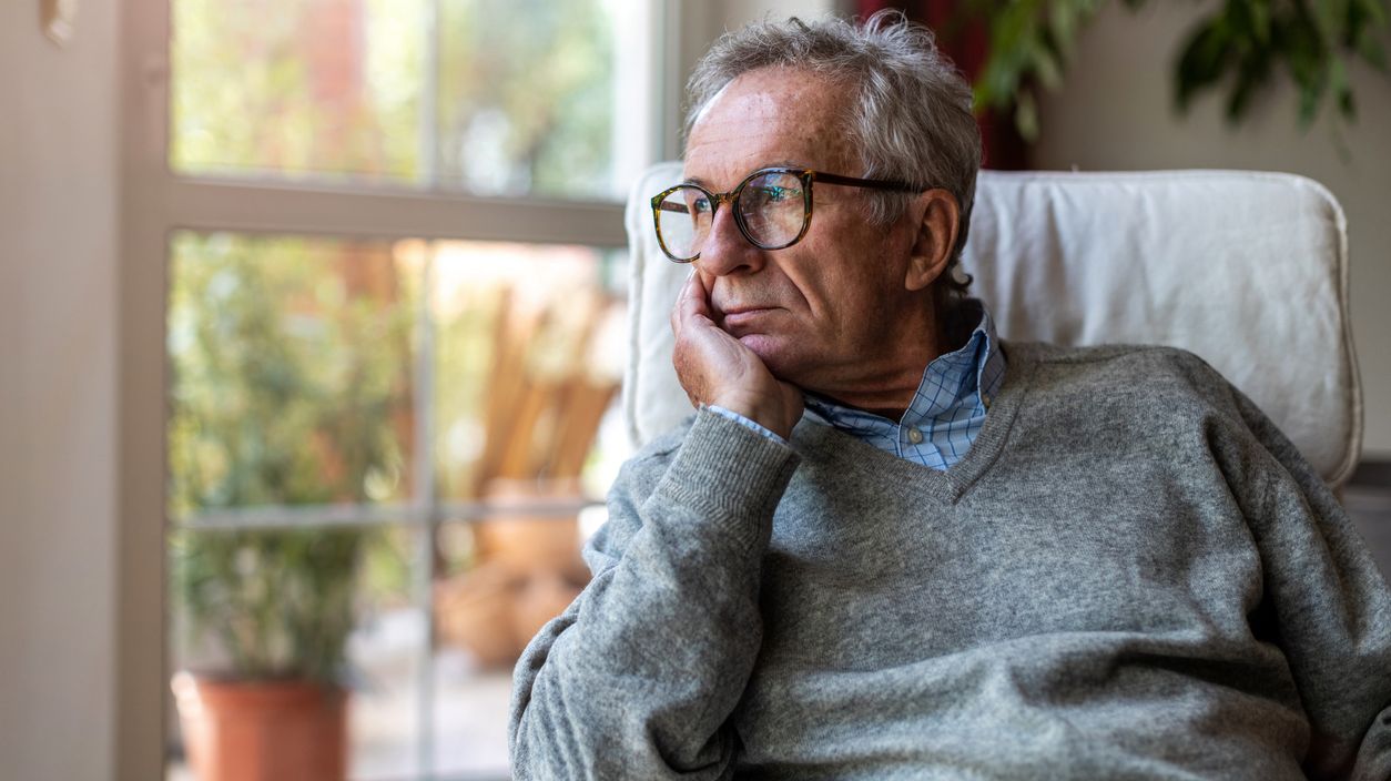 Älterer Mann mit gelangweiltem Gesichtsausdruck schaut aus einem Fenster.