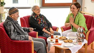 Eine Pflegekraft spricht am Kaffeetisch mit zwei älteren Menschen