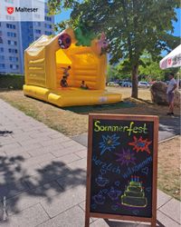 Ein Hinweisschild zum Sommerfest steht vor einer gelben Hüpfburg.