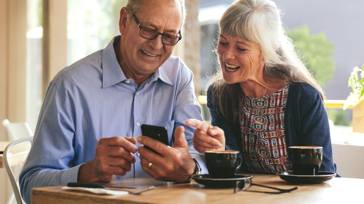 Ein älteres Paar sitzt in einem Café mit Smartphone.