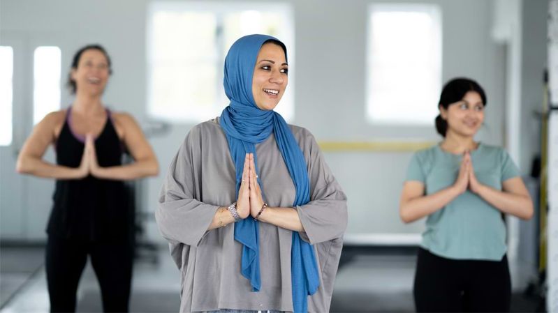 Drei Frauen praktizieren gemeinsam Yoga, eine davon trägt ein Kopftuch.