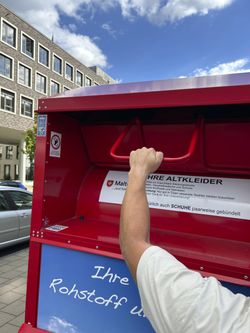 Foto: Ein Malteser Altkleidercontainer wird geöffnet. Zu sehen ist nur der Arm des Spenders.(Quelle: Malteser)