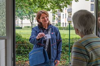 Ältere Dame öffnet die Haustür für die Mitarbeiterin der Malteser. 