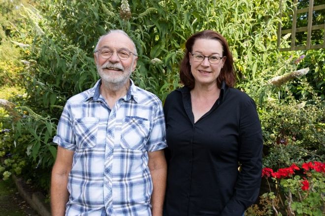 Zwei Personen sehen nebeneinander und lächeln in die Kamera
