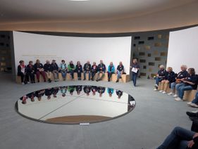 Im Kolumbarium sitzen die Ehrenamtlichen auf Holzbänken unter einem großen, kreisrunden im Boden eingelassenen Spiegel, der das Tageslicht und damit den Himmel aus einer gleichgroßen Öffnung über ihm reflektiert