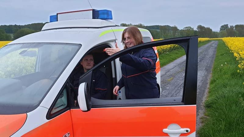 Malteser Mitarbeiterin spricht mit einem Fahrer eines Malteser Dienstfahrzeugs. 