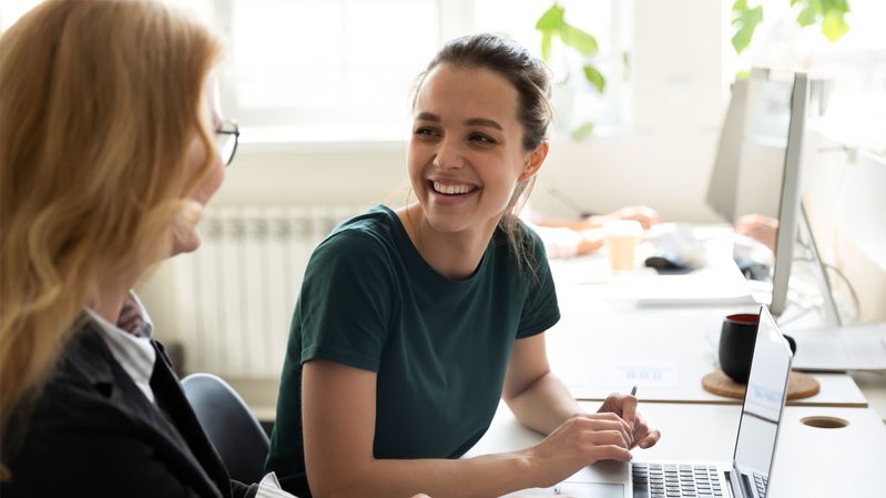 Zwei junge Frauen sitzen vor einem Computer und lachen sich an 