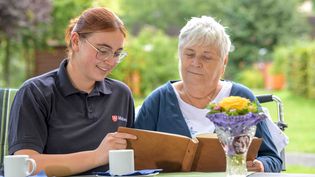 Pflegeeinrichtung der Malteser. Junge Malteserin liest älterer Dame aus der Speisekarte vor.