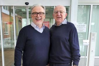 Zwei ältere Männer stehen vor einem Klinikgebäude mit automatischer Glastür.