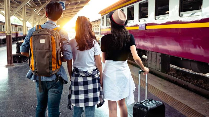 Drei Personen stehen mit ihrem Reisegepäck an einem Bahnhof.