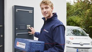 Junger Mann mit Warmhaltebox klingelt an einer Haustür.