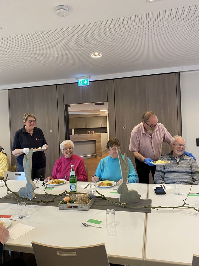 Malteser Helfer servieren den Gästen die Hauptmahlzeit an einem dekorierten Tisch