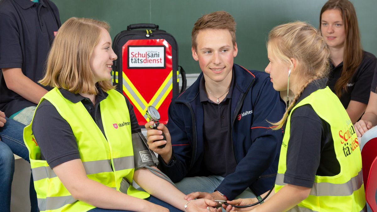 Malteser Schulsanitäter üben im Klassenraum das Blutdruckmessen.