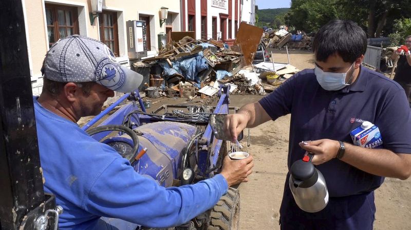 Ein junger Mann mit Mund-Nasen-Schutz schenkt einem Mann auf einem Räumfahrzeug einen Kaffee ein.