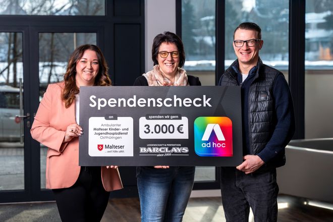 Drei Personen stehen in einem modernen Innenraum und halten gemeinsam einen großen Spendenscheck. Auf dem Scheck steht eine Spendensumme von 3.000 Euro zugunsten des „Malteser Kinder- und Jugendhospizdienstes Ostthüringen“. Logos der Malteser, von Barclays sowie von „ad hoc“ sind ebenfalls zu sehen. Im Hintergrund fällt Tageslicht durch große Fenster.