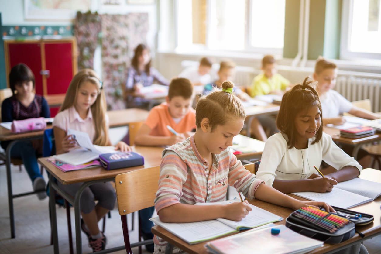 Klassenzimmer: Kinder sitzen an ihren Tischen und schreiben in ihren Heften