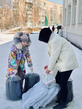 Ein Kind und eine Frau mit Schlafsäcken und Decken im Schnee. Foto: Avalyst/Malteser