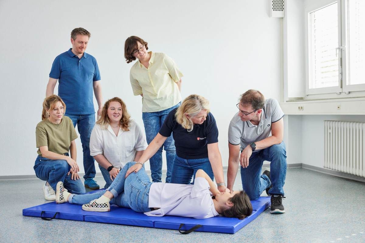 Erste-Hilfe-Kurs der Malteser im nördlichen Breisgau: Eine Ausbilderin zeigt die stabile Seitenlage, während die Teilnehmenden aufmerksam zuschauen und praktisch üben – praxisnahe Ausbildung für Notfallsituationen