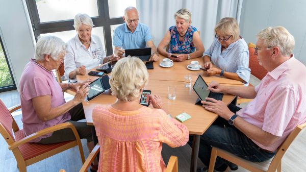 Ältere Menschen mit Kaffeetassen, Tablets und Smartphones an einem Tisch.