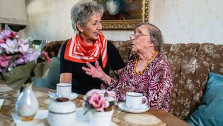Eine ältere ehrenamtliche Malteserin vom Besuchsdienst sitzt zusammen mit einer älteren Dame am Kaffeetisch. Die ältere Dame erzählt die andere hört zu.