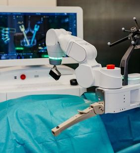 OP-Roboterarm steht über einem abgedeckten Operationstisch, im Hintergrund ist ein Monitor zu sehen.