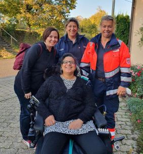 Eine Frau im Rollstuhl. Drei Frauen dahinter. Alle lächeln.
