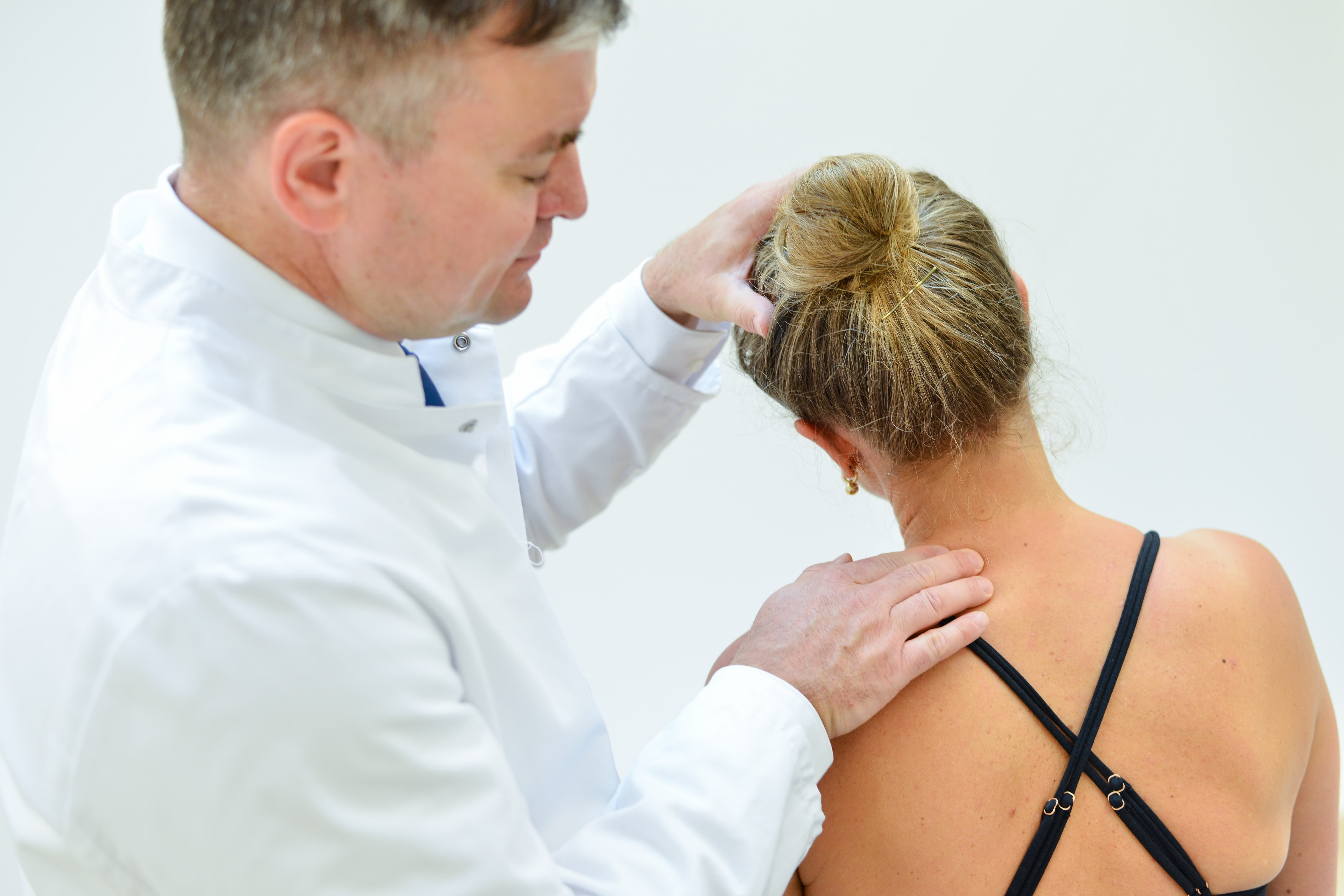 Ärztliche Fachkraft untersucht den Schulter- und Nackenbereich einer Patientin in der Sprechstunde.