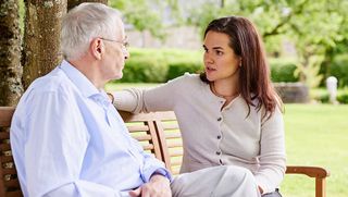 Eine jüngere Frau berät einen älteren Mann zur Patientenverfügung. Sie sitzen im Garten auf einer Bank.