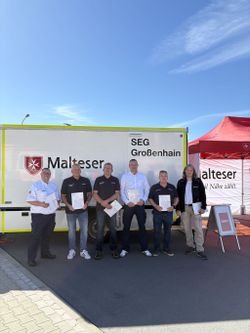 Sechs Malteser stehen mit Urkunden in der Hand vor einem großen Einsatzfahrzeug.