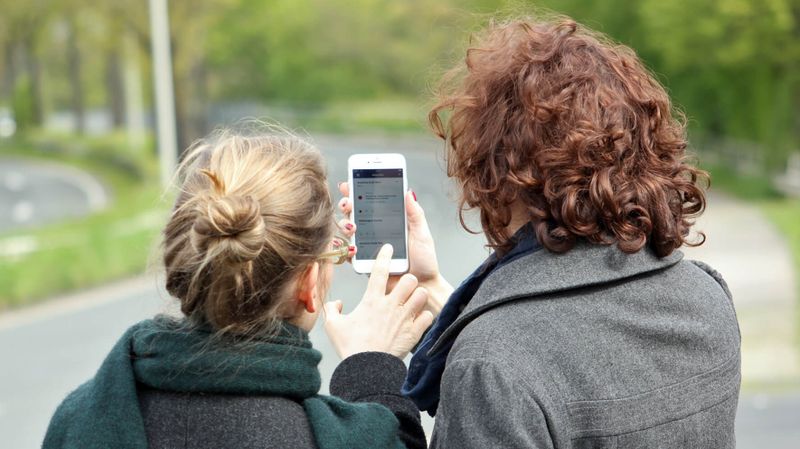Zwei Frauen schauen auf ein Smartphone, auf dem die Benutzeroberfläche der Warn-App NINA zu sehen ist.