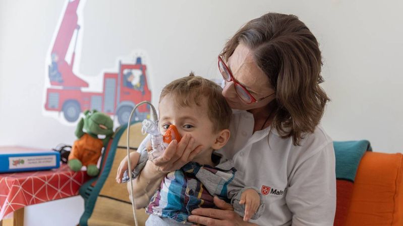 Eine Pflegefachkraft hält Luka auf dem Arm und unterstützt ihn bei der Beatmung.