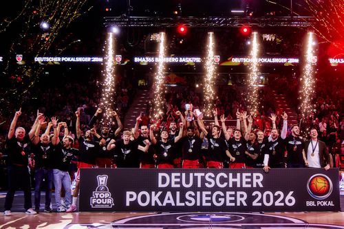 Das Team der Bamberg Baskets jubelt und feiert mit einem Banner "Deutscher Pokalsieger 2026", Medaillen und einem Pokal.