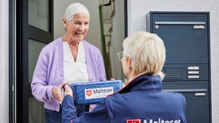 Eine Dame empfängt den Malteser Menüservice an der Haustüre
