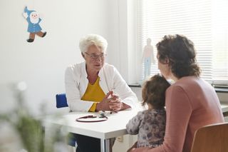 Eine Frau mit ihrem Kind spricht mit einer Ärztin in einer Praxis.