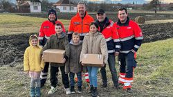 Vier Männer in Malteserkleidung stehen hinter vier Kindern und Jugendlichen, von denen zwei ein Hilfspaket in der Hand halten.