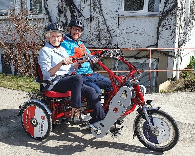 Ein Malteser Helfer fährt mit einer Seniorin Dreirad-Tandem.