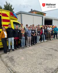 Eine große Gruppe an jungen Menschen steht vor den RTW der Malteser.