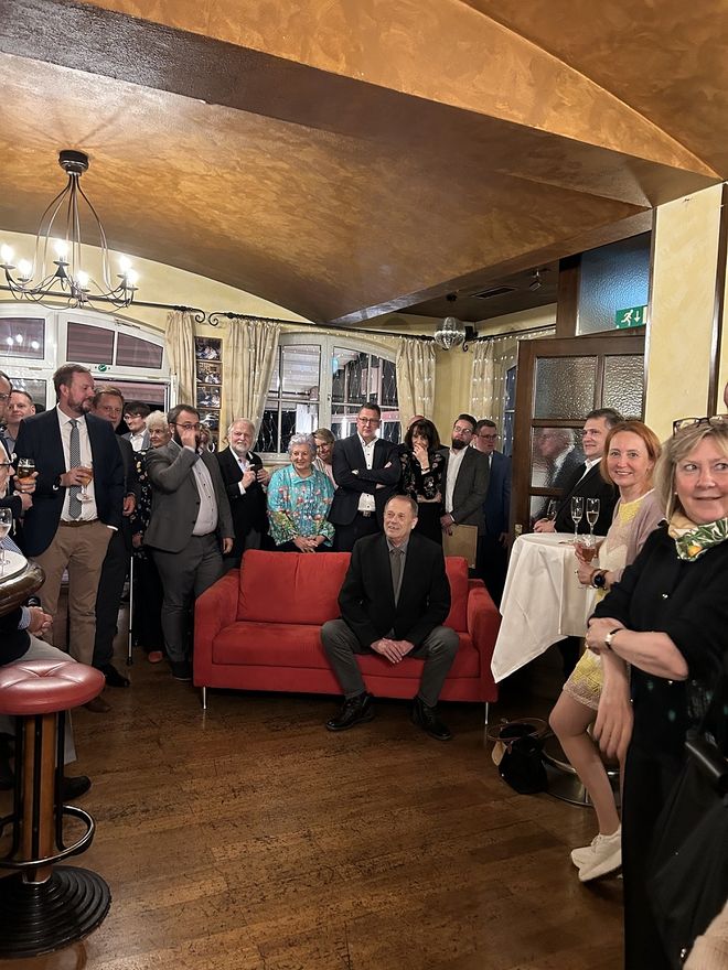 Axel Lemmen sitzt inmitten seiner Gäste auf einem roten Sofa 