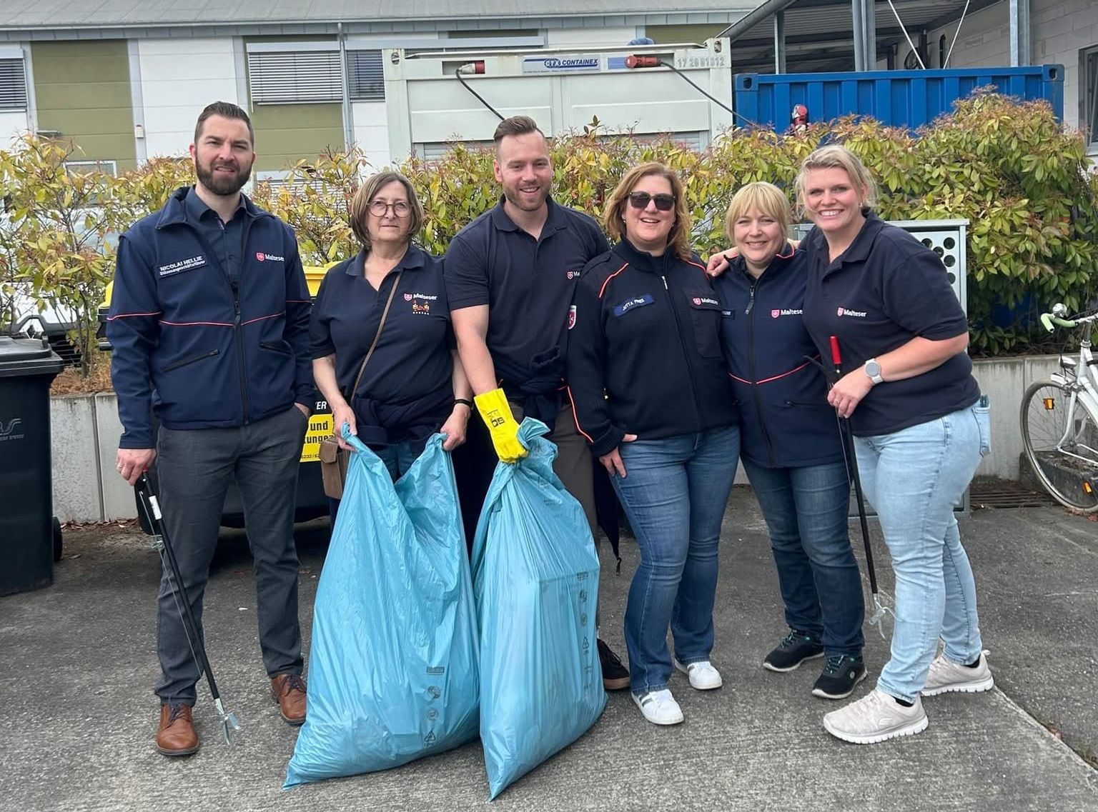 Menschen in Malteserjacken mit vollen Müllsäcken lächeln in die Kamera