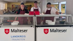 Drei Malteser Helfer stehen hinter einer Theke zur Essensausgabe.