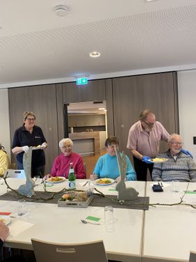 Malteser Helfer servieren den Gästen die Hauptmahlzeit an einem dekorierten Tisch