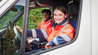 Eine Rettungssanitäterin am Steuer eines RTWs. Im Hintergrund ein Kollege. 