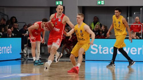 Spieler der Bamberg Baskets im roten Trikot im Angriff gegen gelb gekleidete Gegner auf dem Spielfeld.