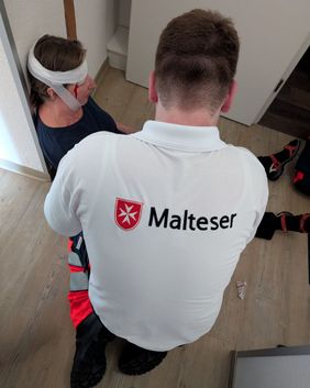 Ein Sanitäter kniet in einer Übung vor einer Patientin mit verbundener (simulierter) Kopfplatzwunde
